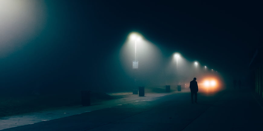 Silhouette of man walking on foggy street at night