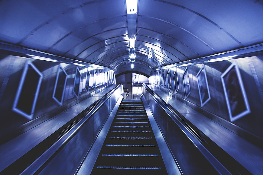 Blue-tinted escalator in a futuristic subway tunnel