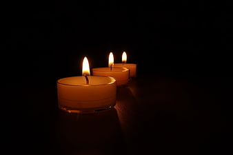 Three lit tea light candles glowing in a dark room