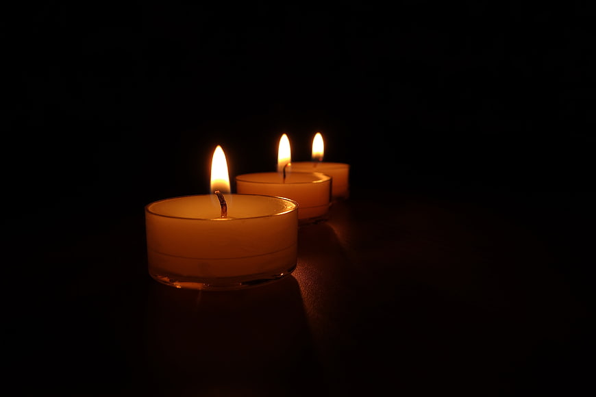 Three lit tea light candles glowing in a dark room