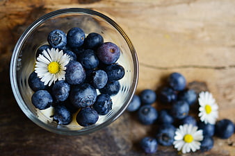 Overhead view of blueberries and daisies in a glass bowl on a rustic wooden table