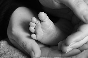 Black and white close-up of a newborn baby's tiny foot held by an adult hand