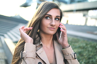 Woman in beige trench coat talking on smartphone outdoors