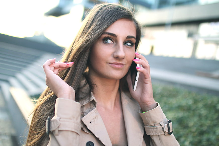 Woman in beige trench coat talking on smartphone outdoors