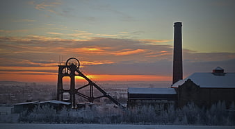 Silhouette of old industrial mine headframe and chimney at sunrise