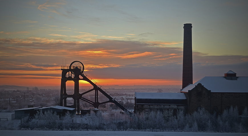 Silhouette of old industrial mine headframe and chimney at sunrise
