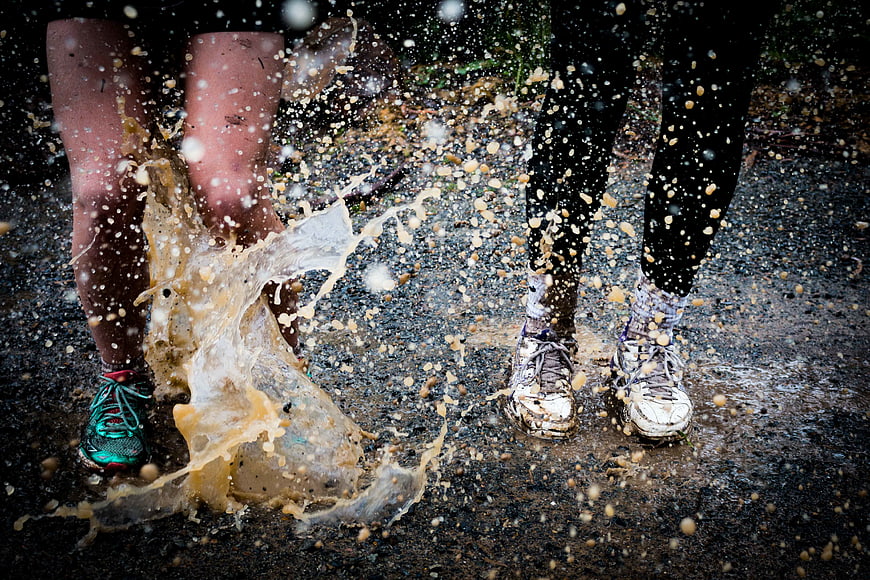 Runners splashing through muddy puddles in rain