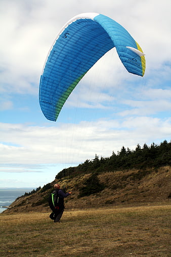 Man Launching Blue Paraglider on Coastal Cliff