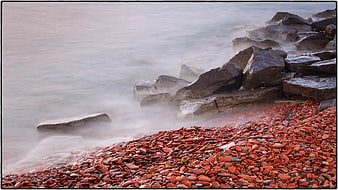 Red Pebble Beach with Misty Ocean and Large Rocks