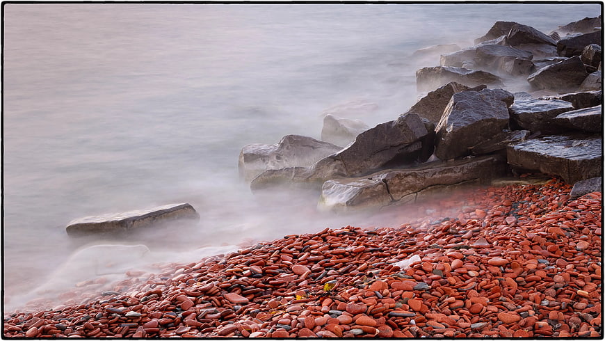 Red Pebble Beach with Misty Ocean and Large Rocks