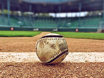 Dirty baseball on dirt field with blurred stadium background
