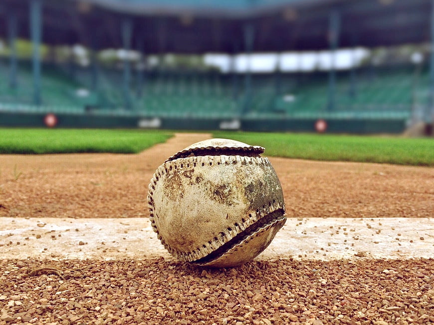 Dirty baseball on dirt field with blurred stadium background