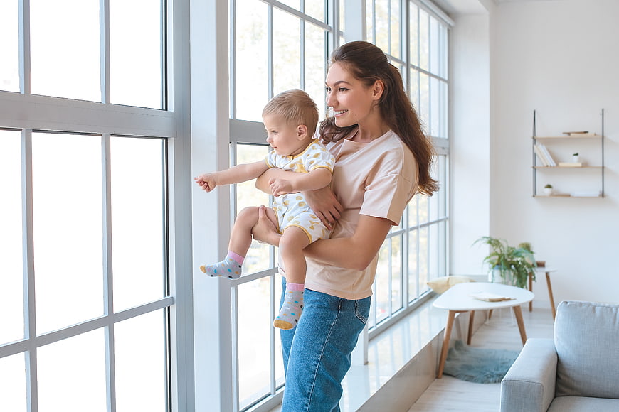 Happy Mother Holding Toddler Boy Looking Out Large Window