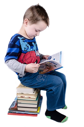 Young boy reading book while sitting on stack of books