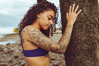 Woman with tattoos leaning against tree on beach