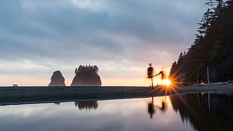 Silhouette of person doing yoga on beach at sunset with rock formations