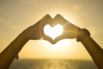 Hands forming heart shape around sunset sun over ocean