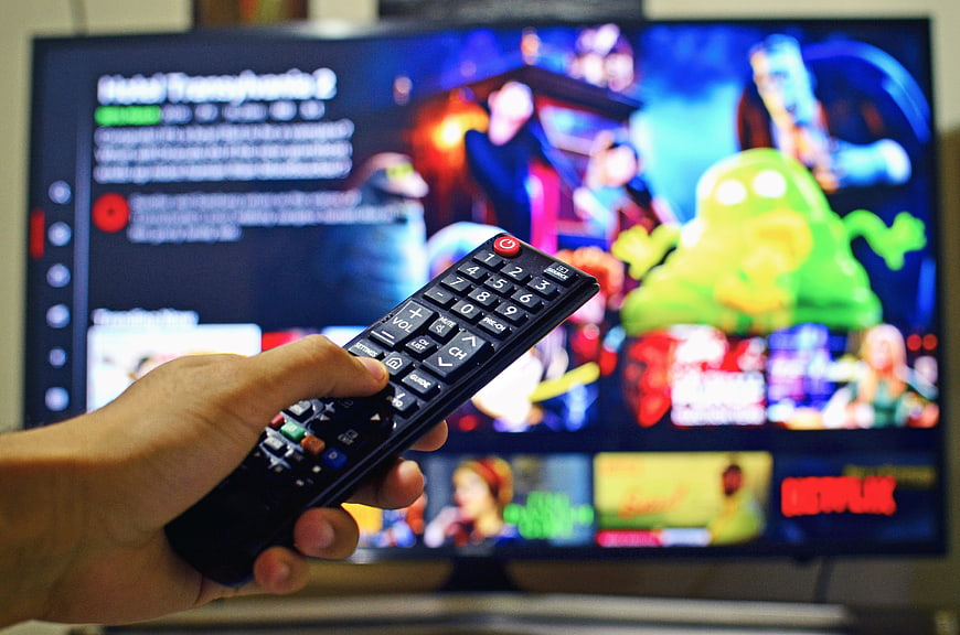 Hand holding remote control pointing at streaming TV interface
