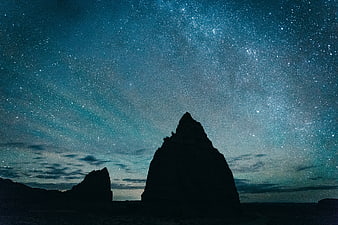 Silhouette of desert rock formation under starry night sky