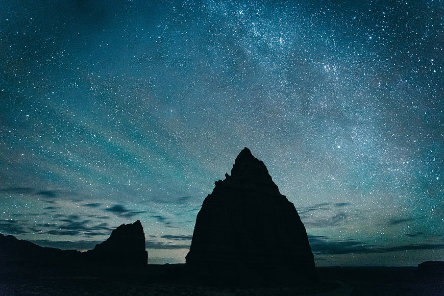 Silhouette of desert rock formation under starry night sky