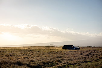 Black SUV driving through dry grassland at sunset