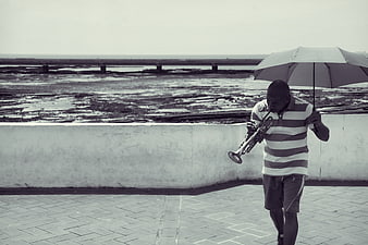 Man playing trumpet with umbrella by the sea