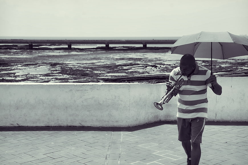 Man playing trumpet with umbrella by the sea