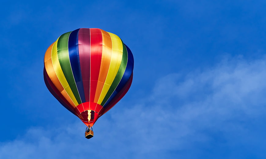 Colorful rainbow hot air balloon floating in a clear blue sky
