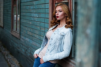 Blonde Woman in Denim Jacket Leaning Against Blue Wooden Wall