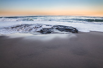 Serene Ocean Waves Crashing on Sandy Beach at Sunset