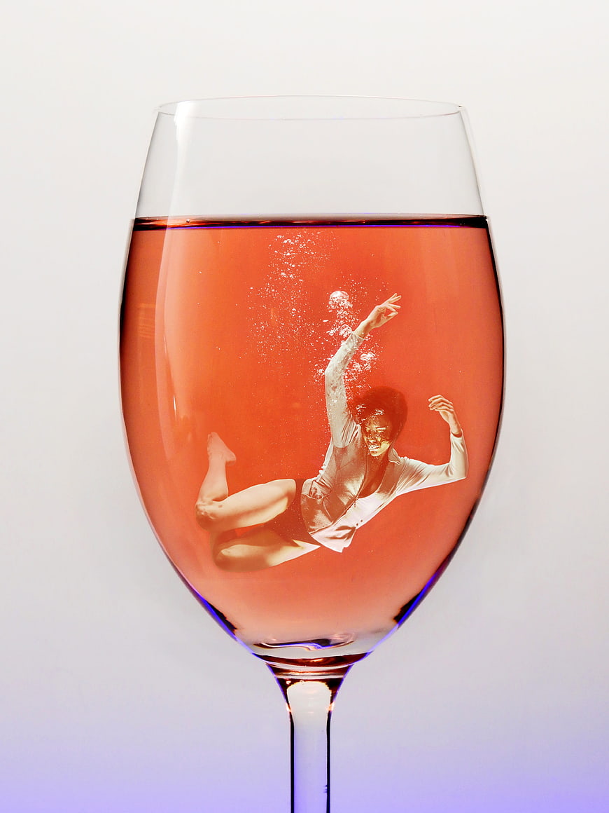 Woman diving into a glass of pink wine