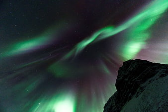 Vibrant green aurora borealis dancing over a snow-capped mountain peak at night
