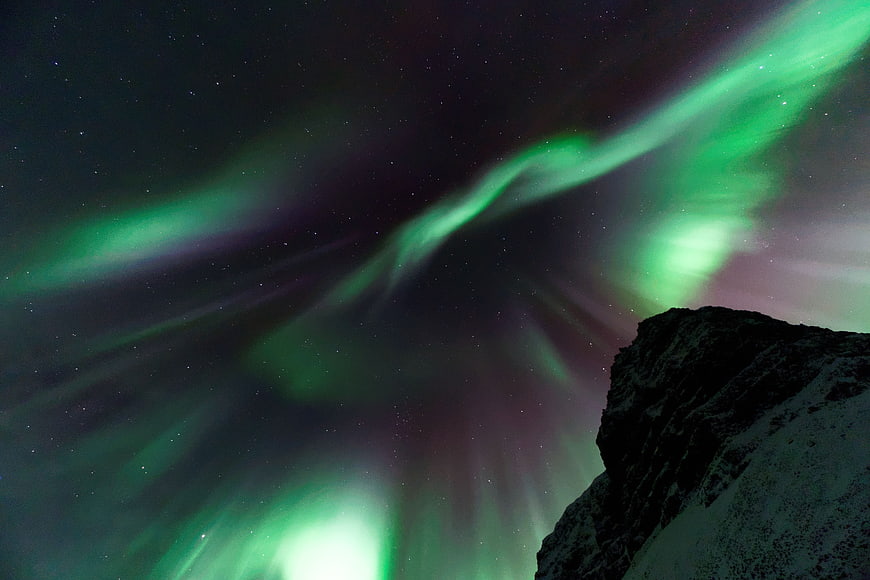 Vibrant green aurora borealis dancing over a snow-capped mountain peak at night