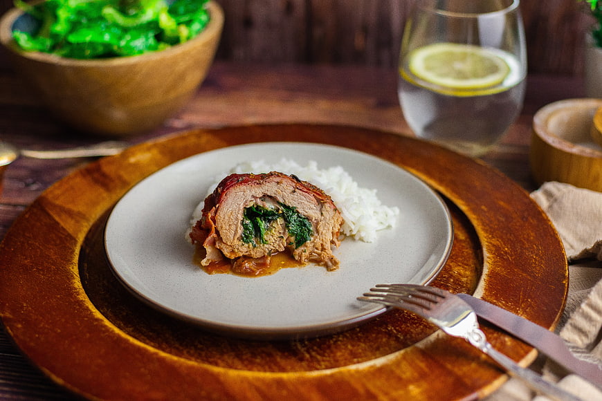Sliced stuffed pork roll with spinach and rice on wooden board