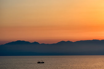 Silhouette of a boat on calm water with mountains at sunset