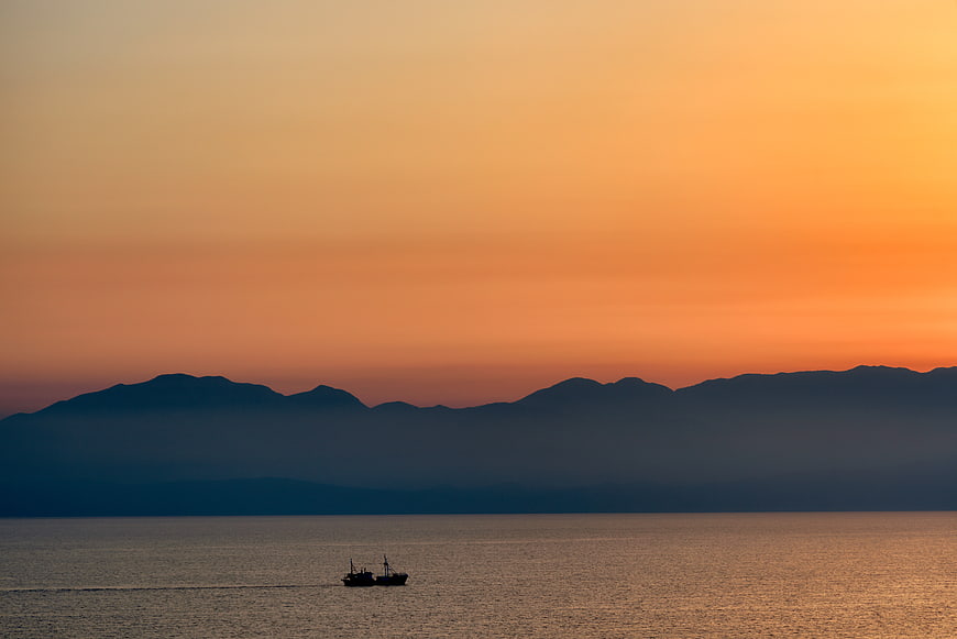 Silhouette of a boat on calm water with mountains at sunset