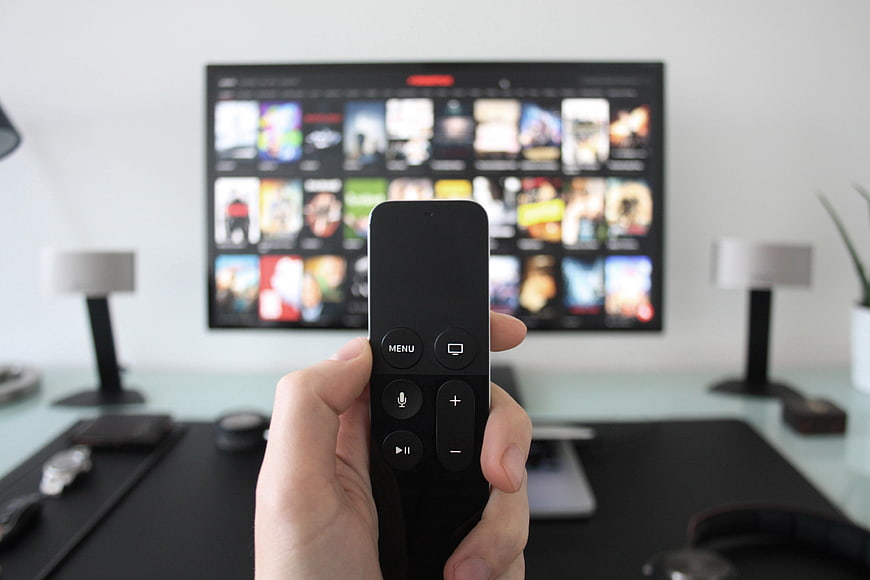 Hand holding remote control pointing at streaming TV screen