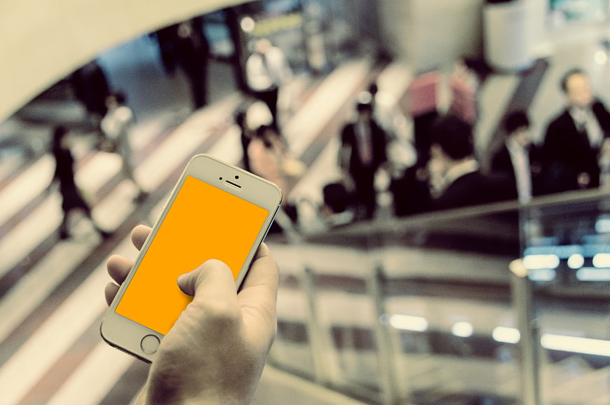 Hand holding smartphone with orange screen in busy business district