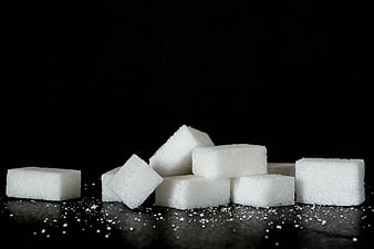 White sugar cubes on black background with granules