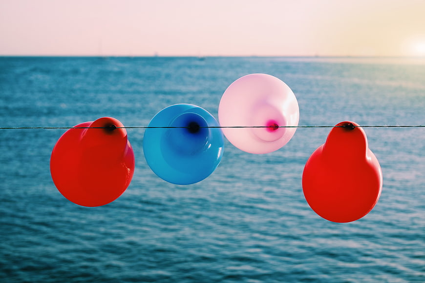 Colorful balloons on a wire against the ocean at sunset