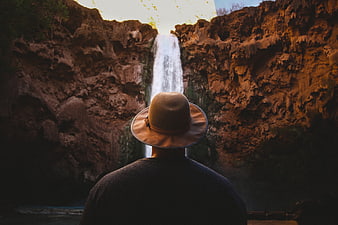 Man in Hat Viewing Waterfall in Canyon