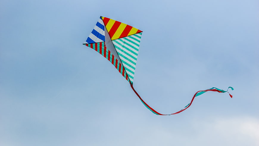 Colorful Striped Kite Flying High In Blue Sky