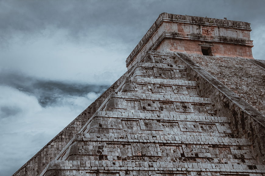 Low angle view of ancient Mayan pyramid ruins against dramatic cloudy sky