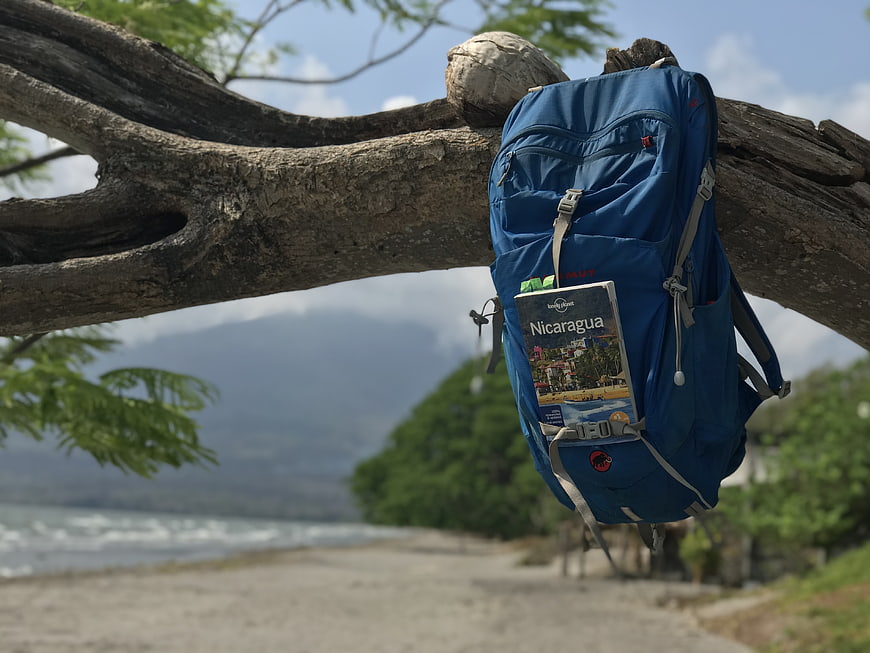 Blue backpack with Nicaragua travel guide hanging on tree branch