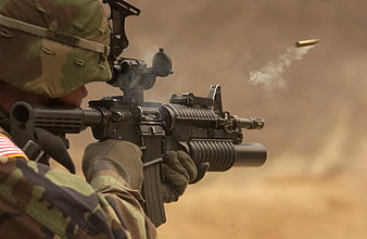 Soldier firing rifle with ejected bullet casing in desert