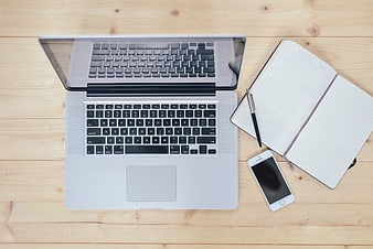 Top-Down View of Open Laptop, Notebook, Pen, and Smartphone on Wooden Desk