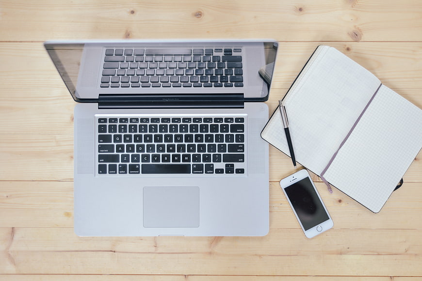 Top-Down View of Open Laptop, Notebook, Pen, and Smartphone on Wooden Desk