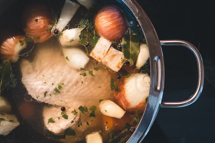 Overhead view of homemade chicken broth simmering in a pot