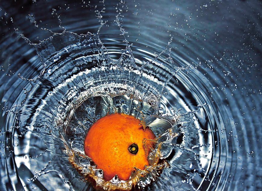 Orange Dropping Into Water With Dramatic Blue Splash