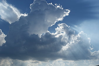 Dramatic cumulus clouds with sun rays in blue sky